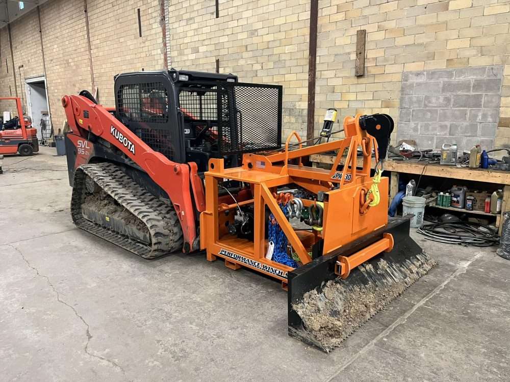Tracked skid steer with a large winch box on the front for towing and recovery.
