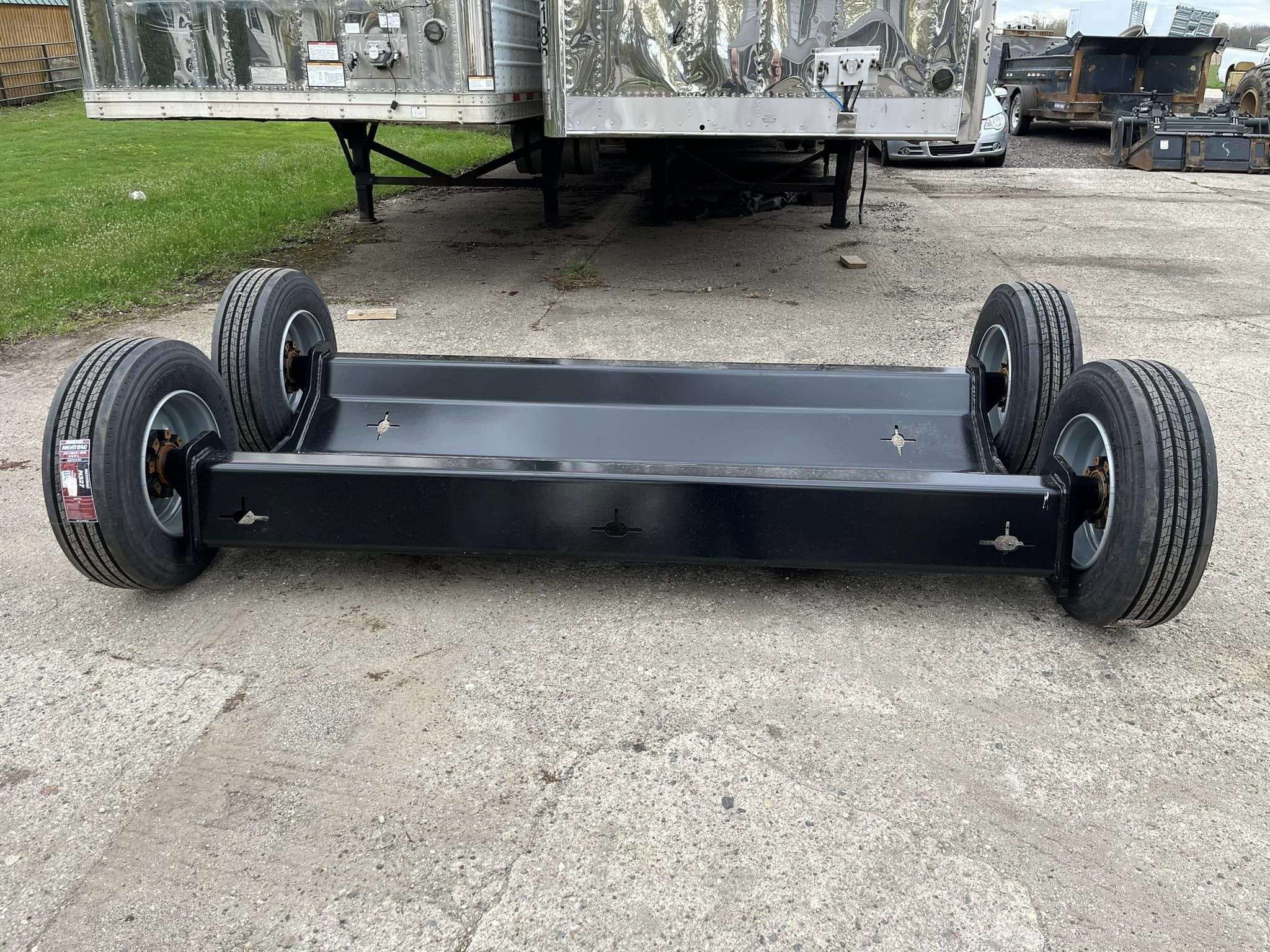 A custom black towing dolly parked in front of two fifty three foot trailers.