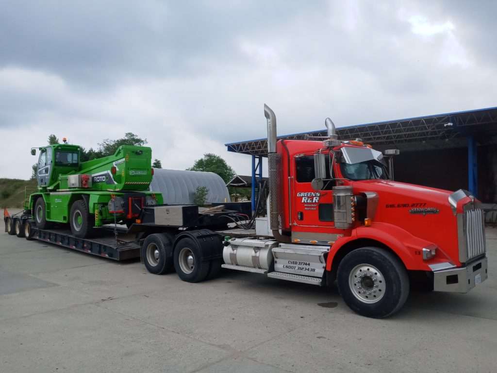 A large tractor trailer hauling a low boy trailer with a large piece of machinery on it.